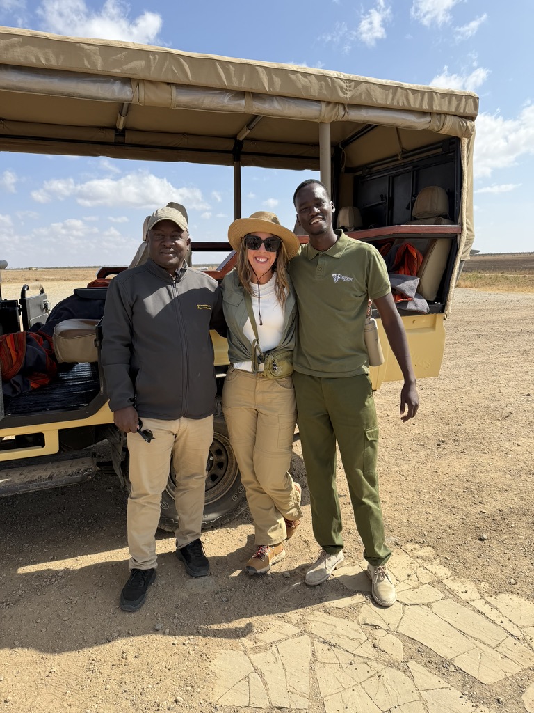 Travel advisor with local safari guides standing beside a safari vehicle in the Maasai Mara, Kenya during a guided game drive experience