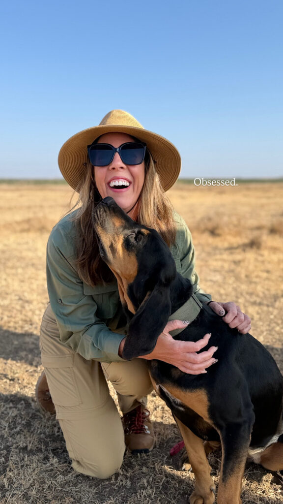 Woman smiling and petting a dog in the Kenyan savanna during a safari experience in Africa